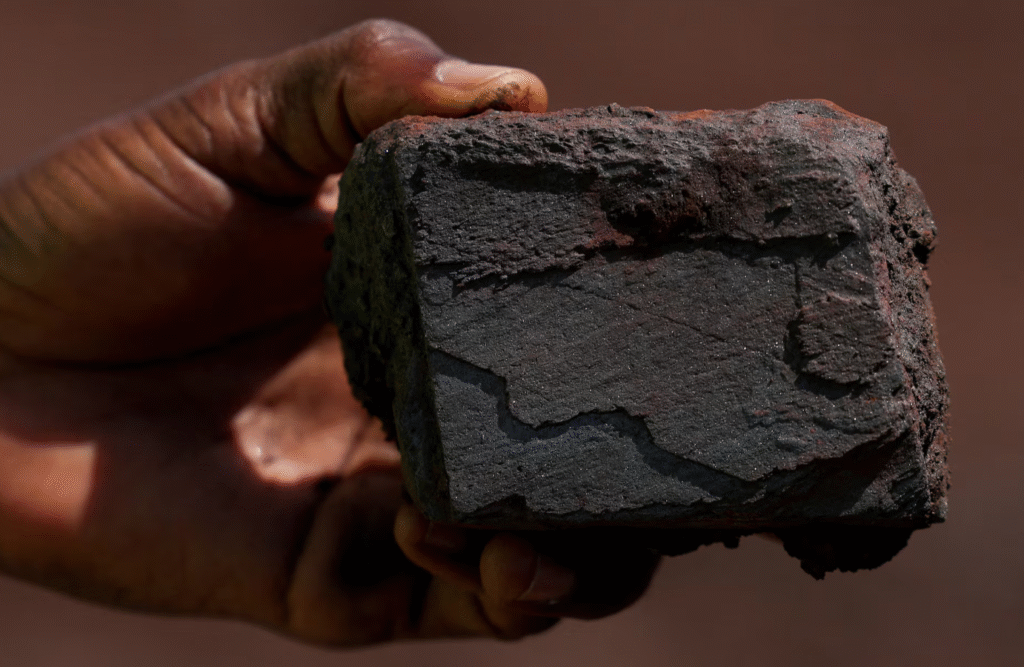 A hand holding a lump of iron ore at the Simandou mine