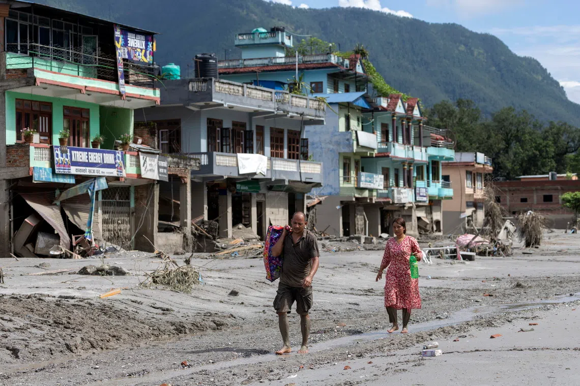 Residents walk barefoot through thick grey mud covering a street in the aftermath of the Nepal-Tibet flash floods.