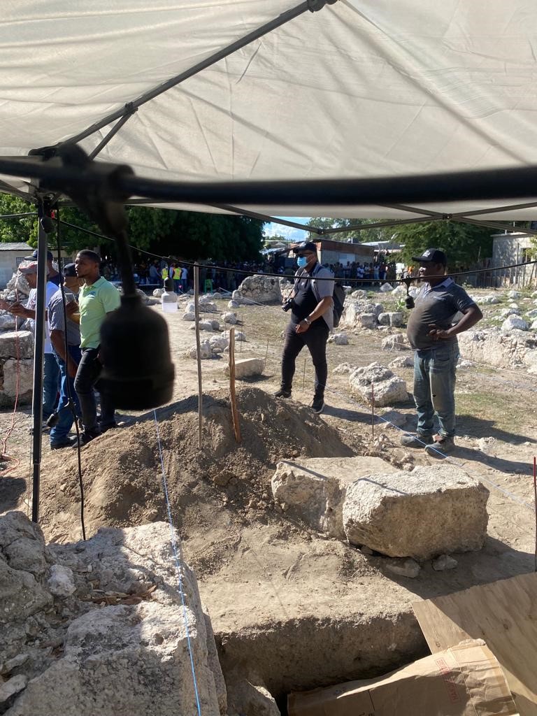 Excavation site under a white canopy with workers and observers