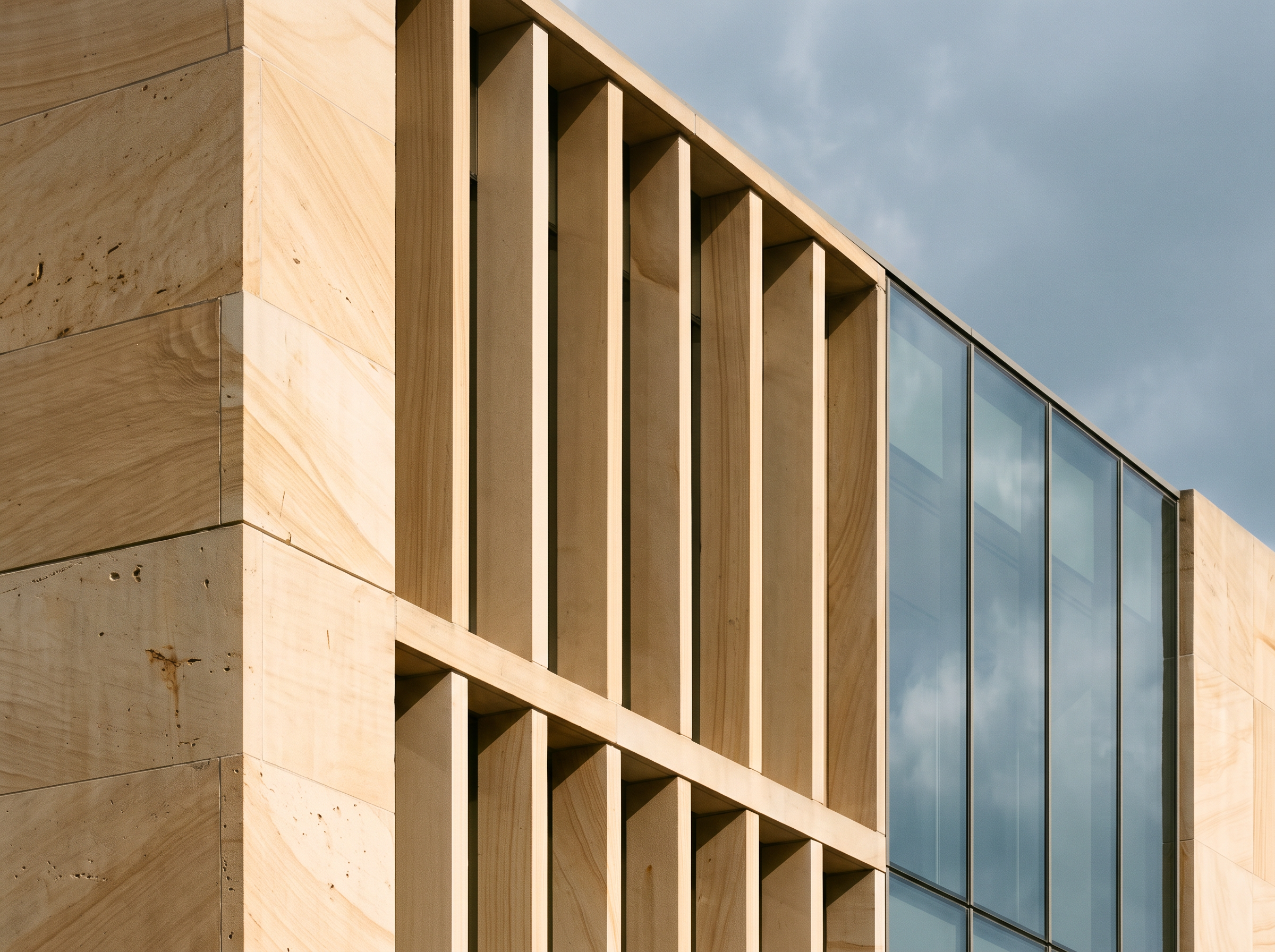 Detalle arquitectónico de piedra arenisca con lamas verticales y vidrio que refleja el cielo
