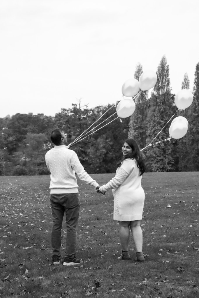 Couple holding white balloons in field black and white maternity