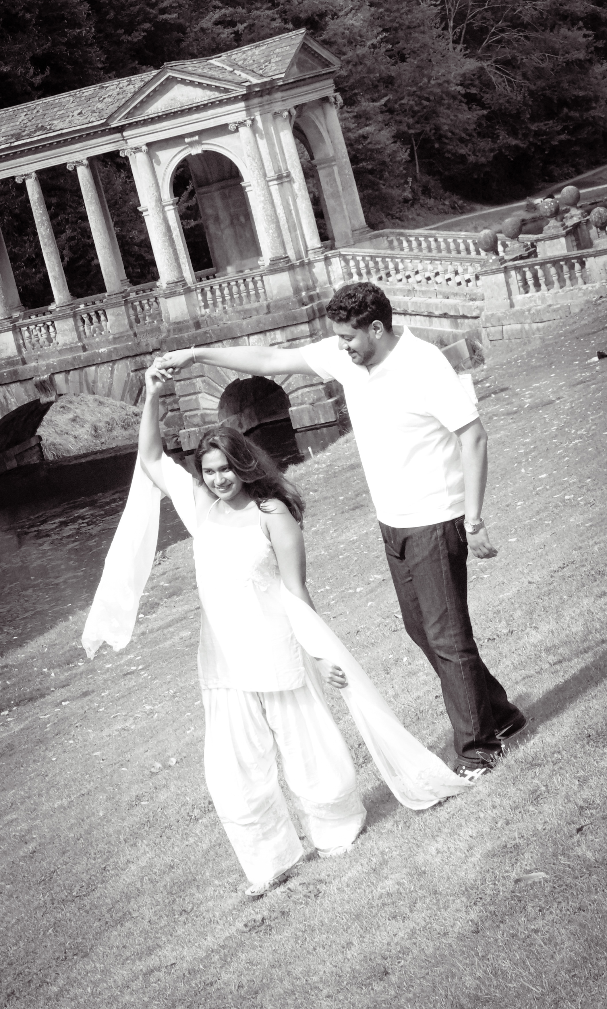Black and white couple on grassy bank with stone bridge behind