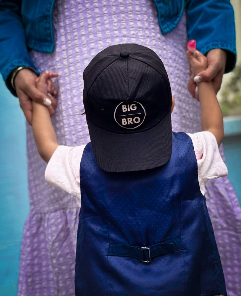 Pregnant woman holding child wearing big bro hat and colorful outfits