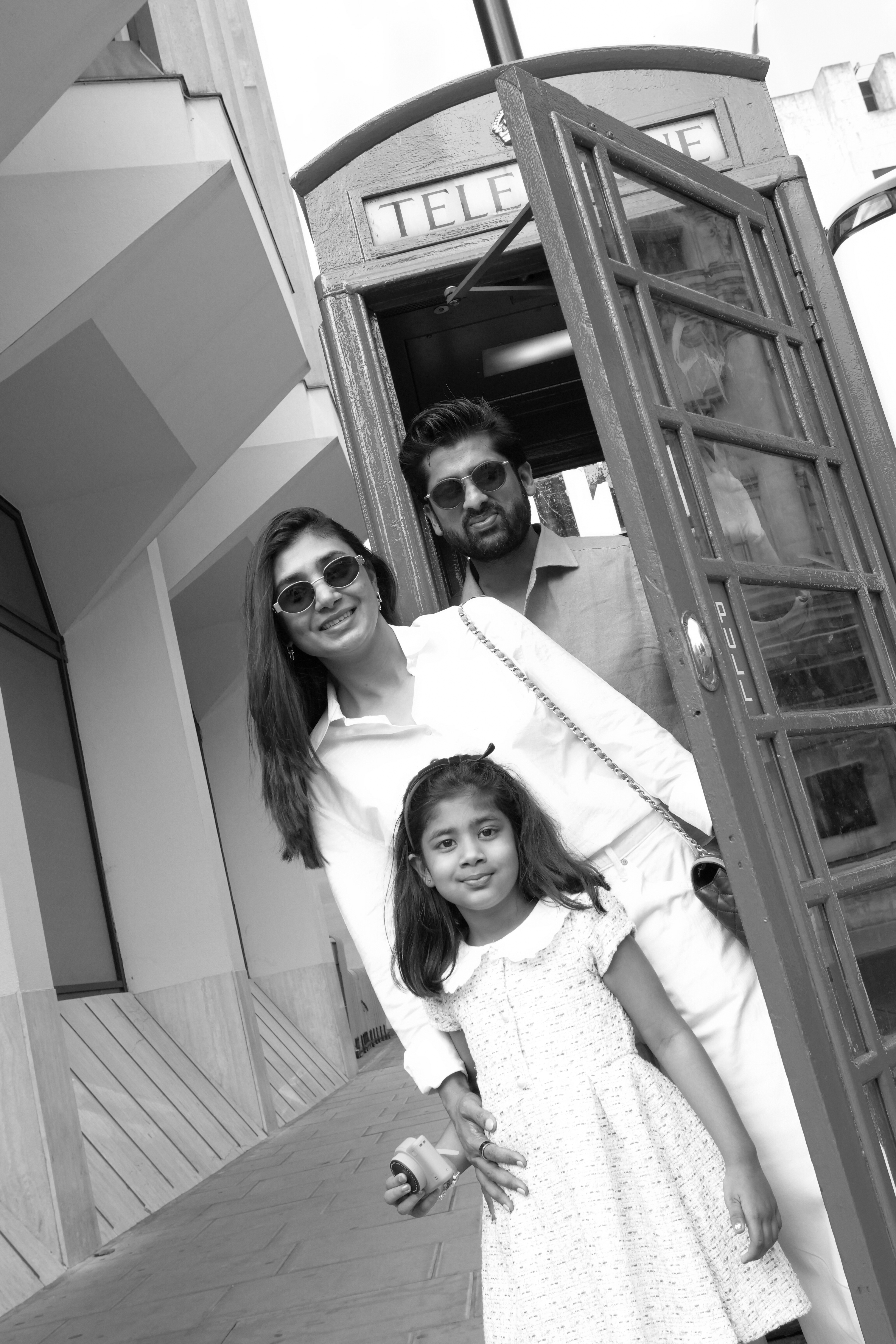 Black and white family beside red telephone box with daughter holding toy camera