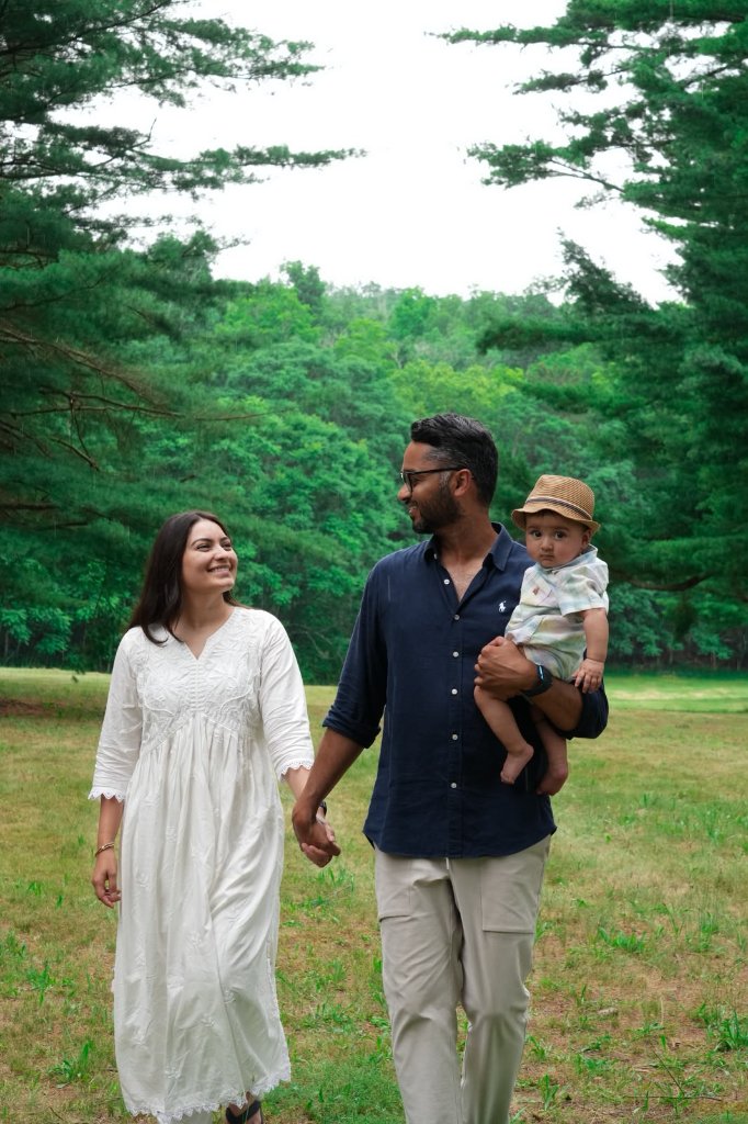 Father carrying baby in hat while walking with mother in park