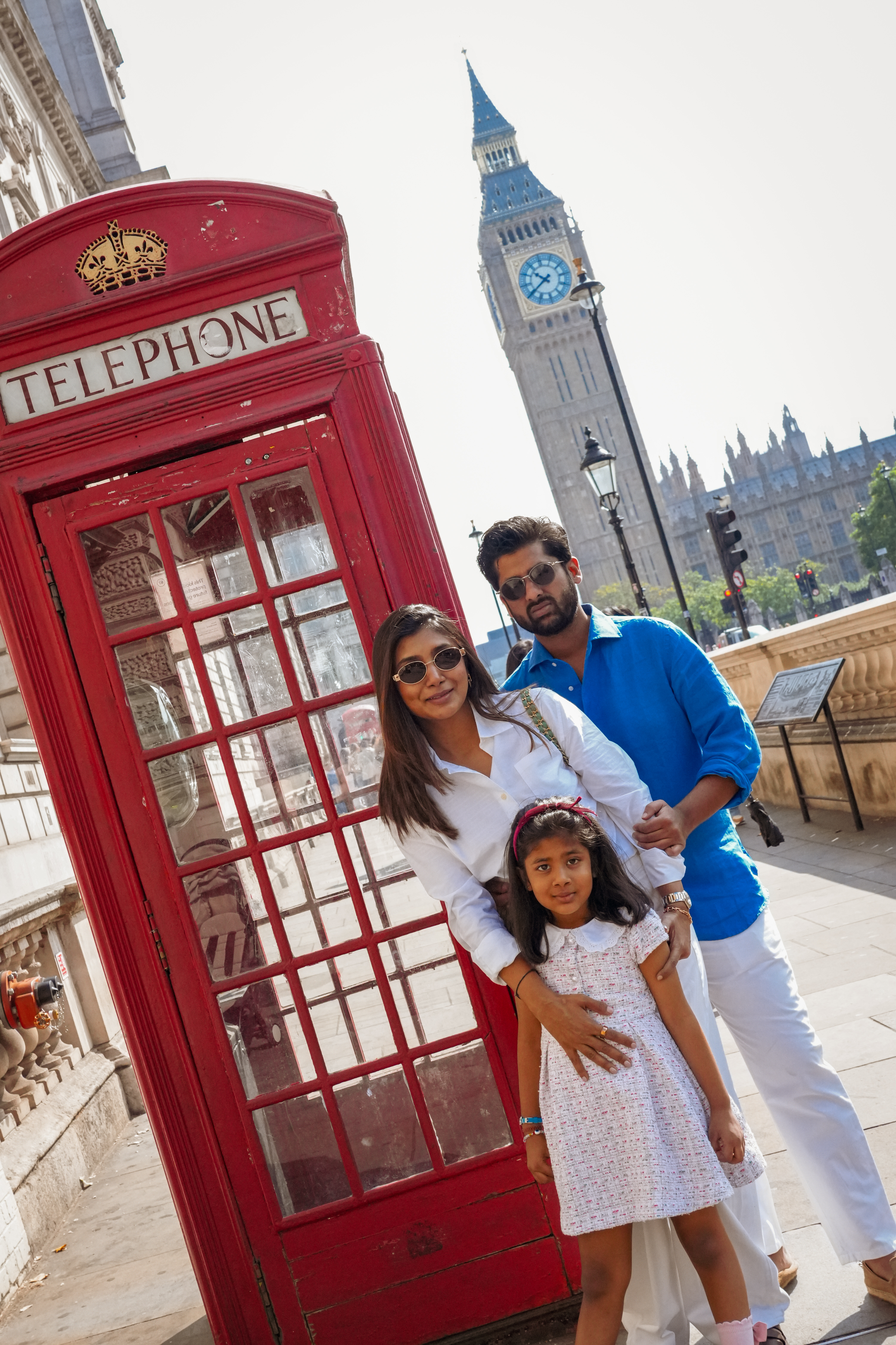 Family of three beside red London telephone box with Big Ben behind