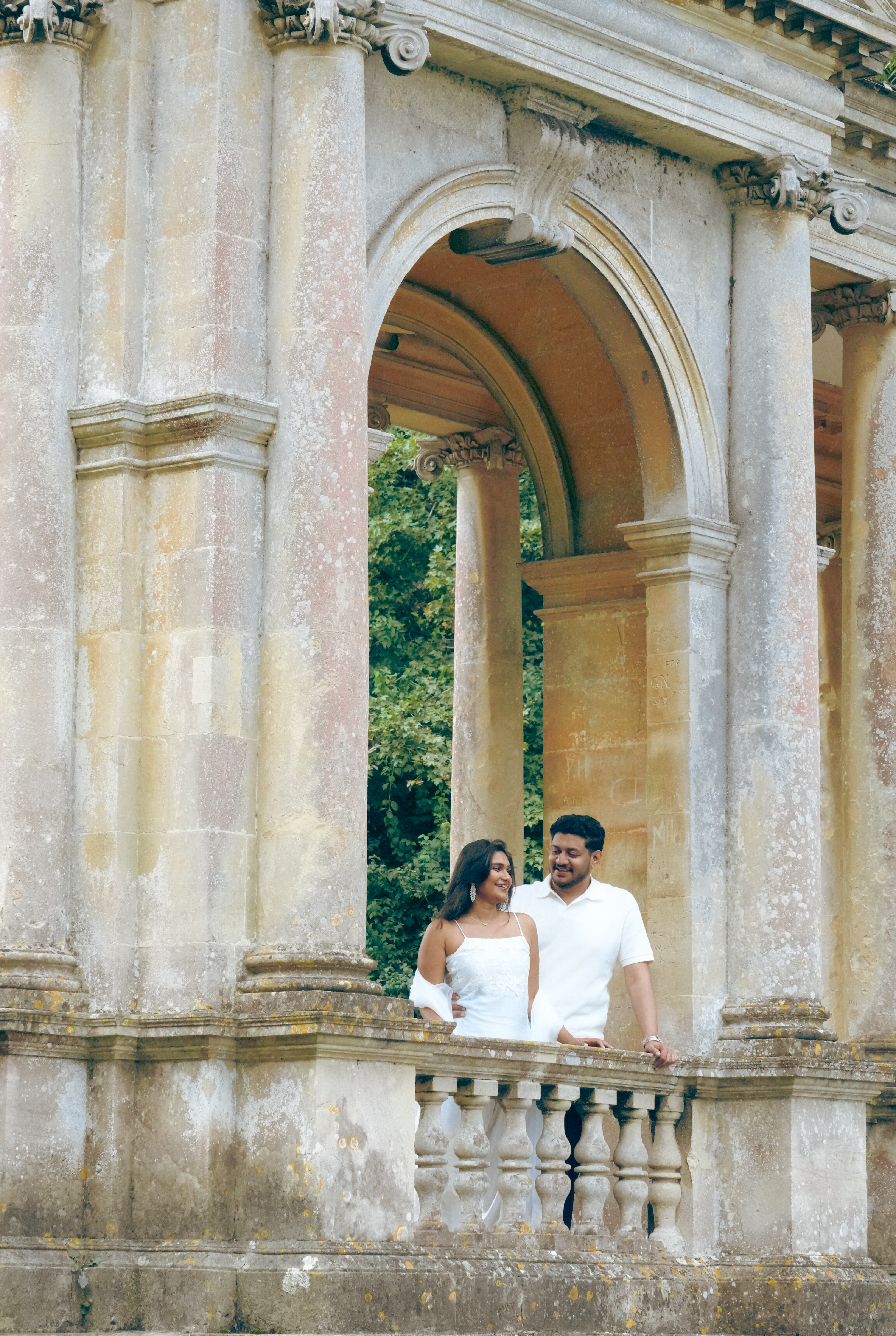 Couple smiling together behind stone balustrade with forest behind