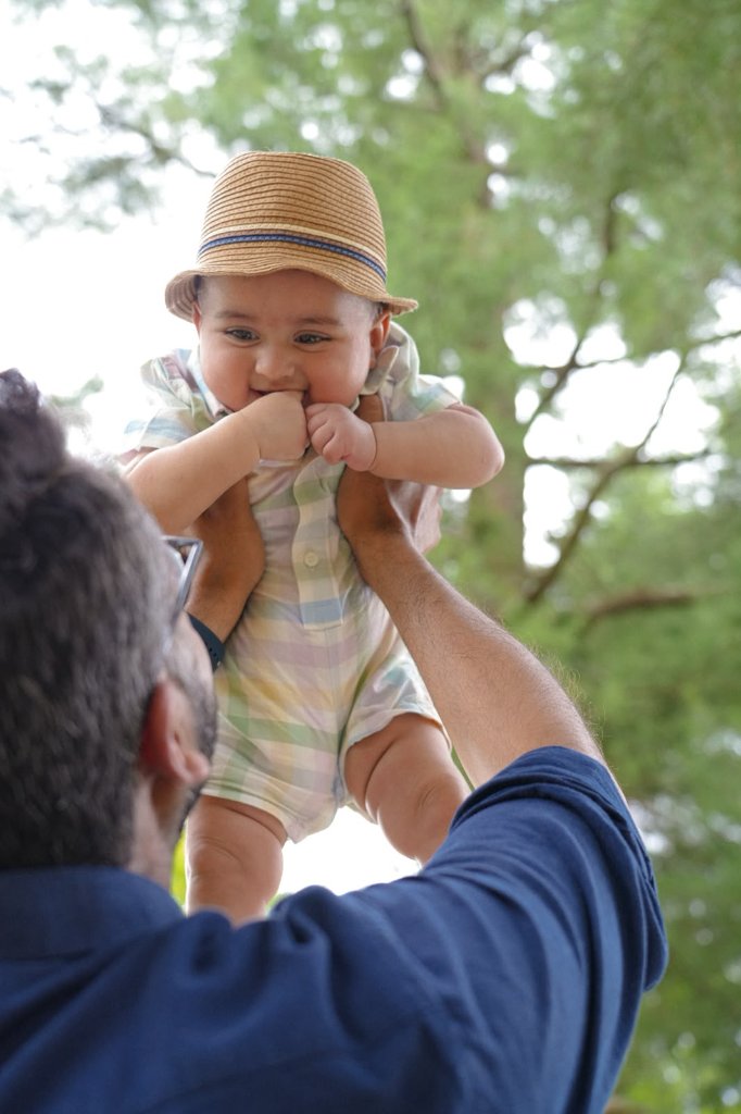 Father holding baby in straw hat up in the air outdoors