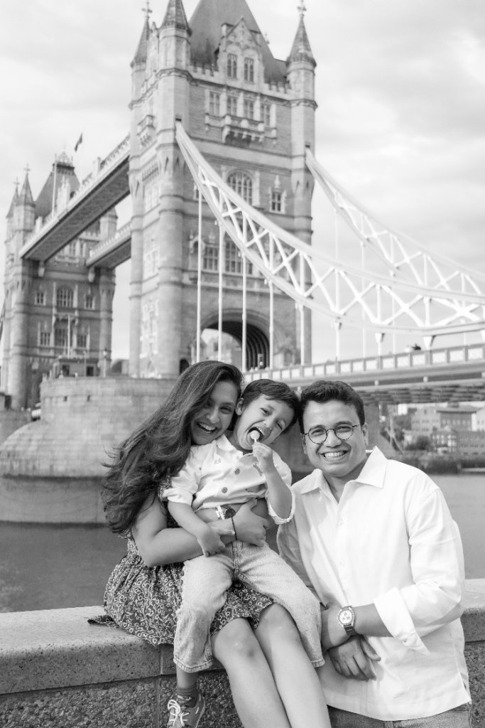 Family of three sitting on stone wall with Tower Bridge behind