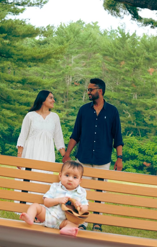 Baby sitting on bench with parents smiling behind in park