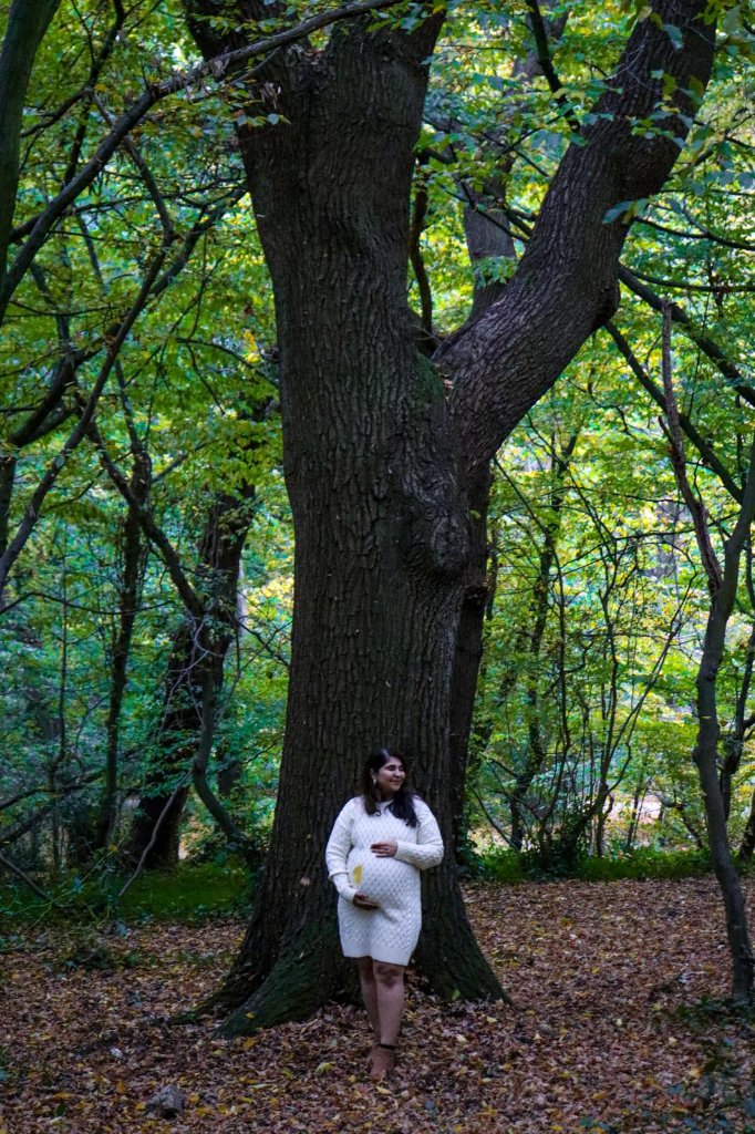 Pregnant woman standing by large tree in autumn woodland