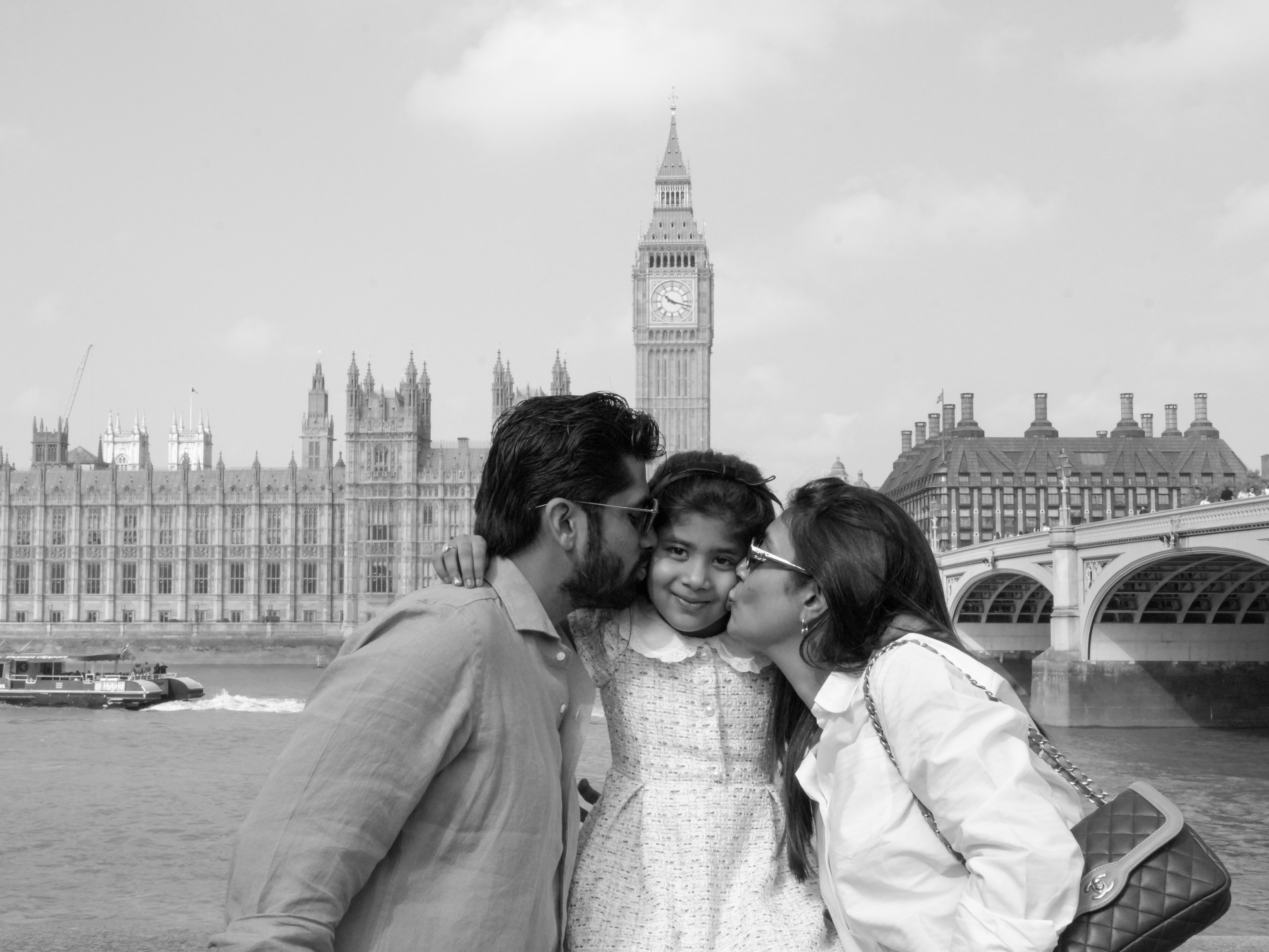Black and white family with parents kissing daughter beside Big Ben