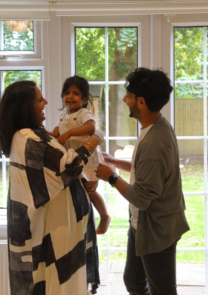 Family laughing together holding toddler by window
