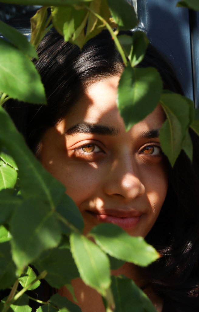 Close up portrait of woman peering through green leaves