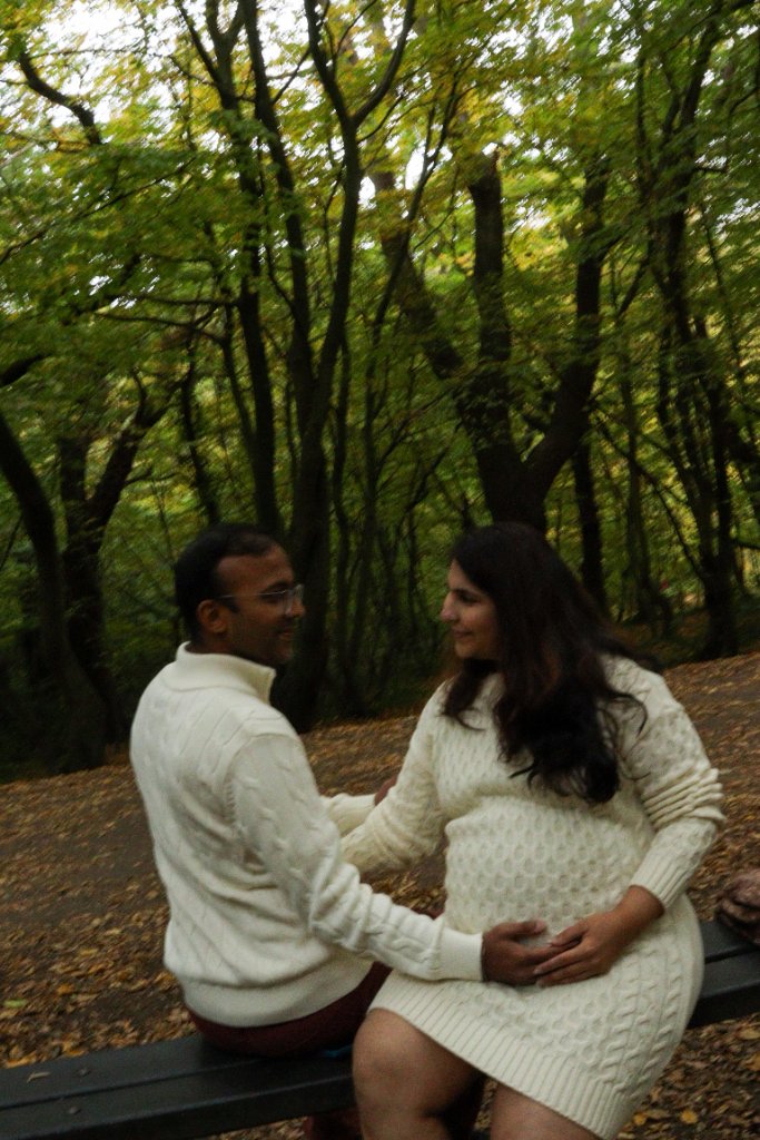 Couple on bench in woodland holding baby bump