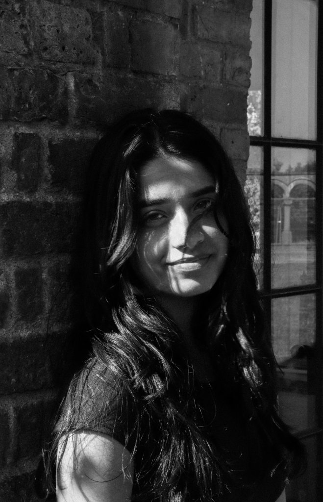 Black and white portrait of woman leaning against brick wall by window