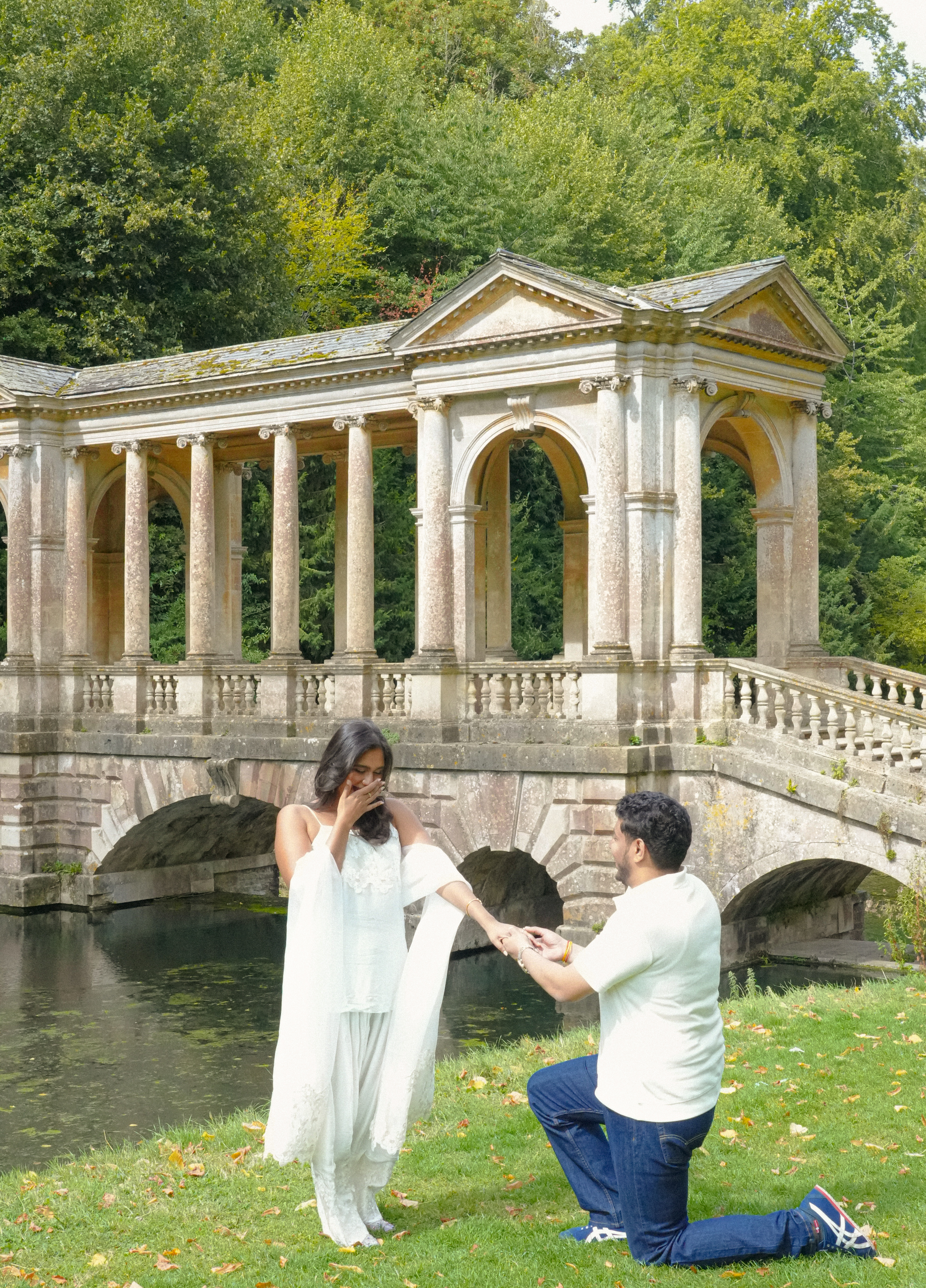 Proposal moment with man on one knee in front of stone bridge