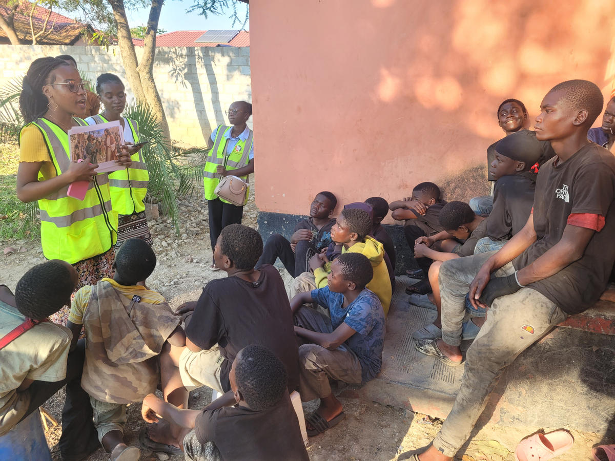 Volunteers sharing an illustrated booklet with children seated outdoors