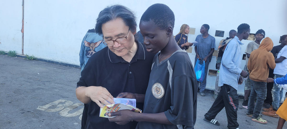 William W. Seo looking at a booklet with a young person during Project Nshima
