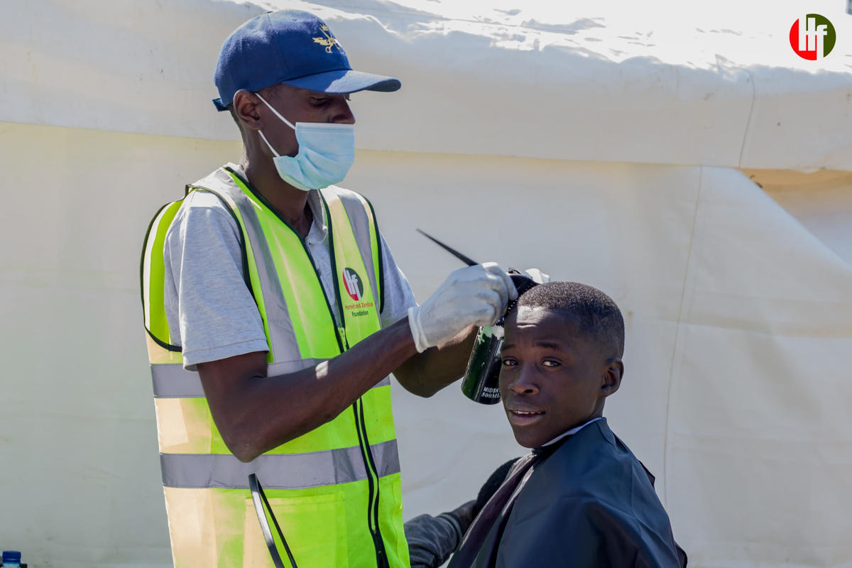 A volunteer tending to a young person's hair outdoors