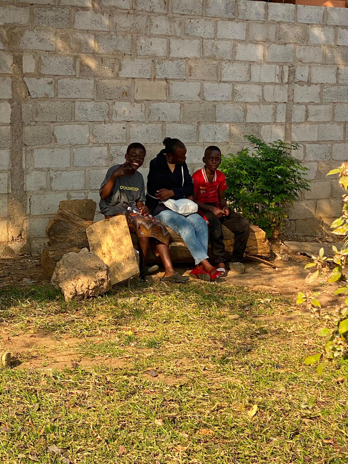 A seated volunteer with two children beside a wall
