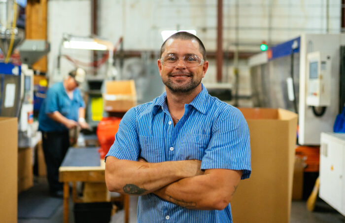 Smiling worker with arms crossed in a manufacturing facility