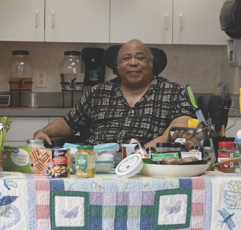 Older woman seated at a kitchen table with food and household items
