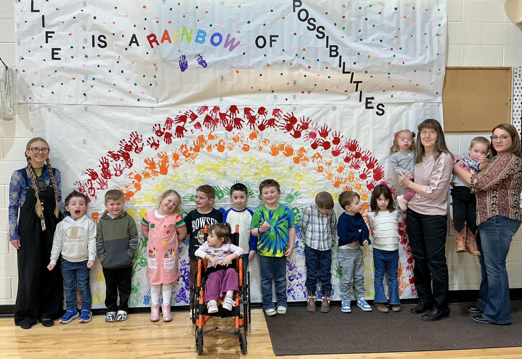 Preschool children and teachers in front of a Life is a Rainbow of Possibilities mural
