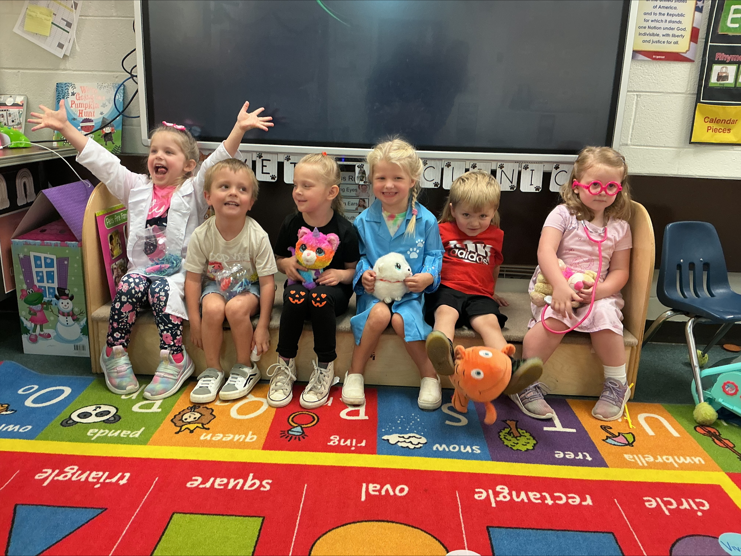 Preschoolers on a classroom bench with arms raised cheering
