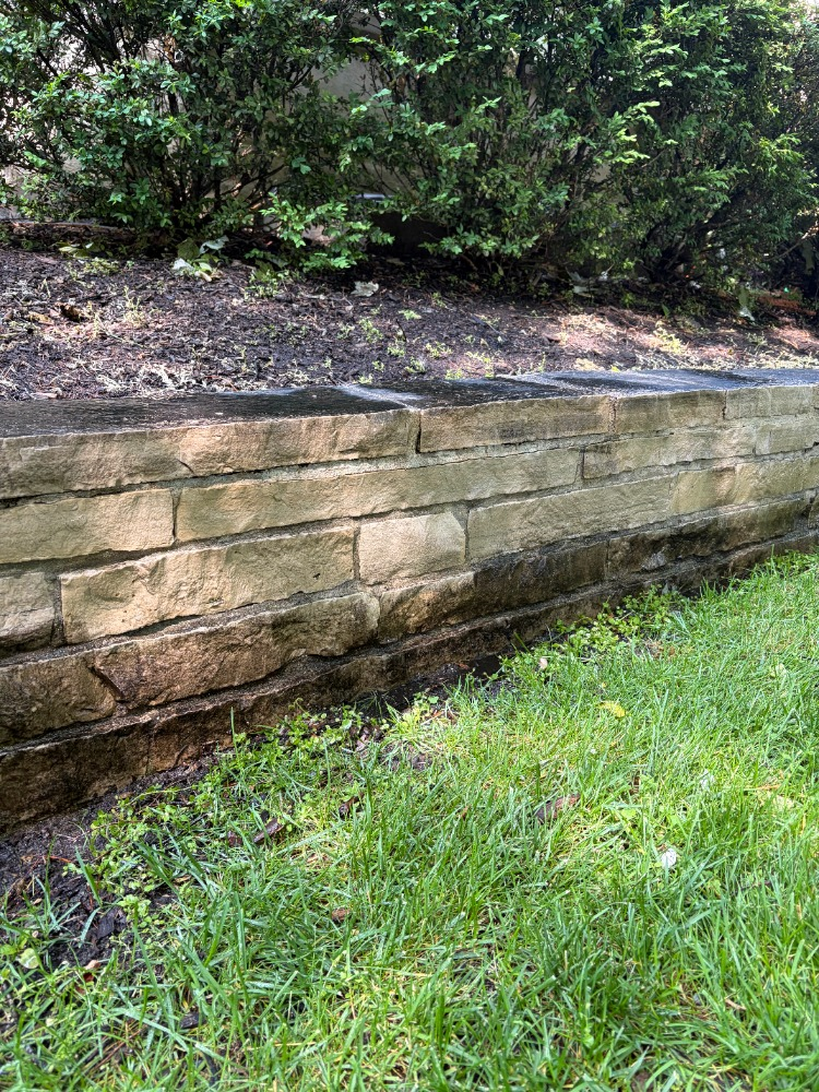 Stone retaining wall with mulch garden bed and green lawn