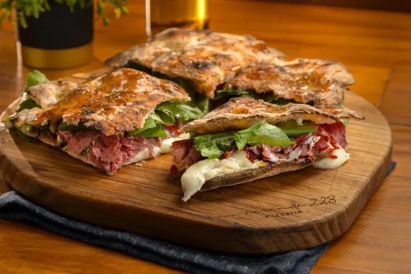 Puccia com pastrami, queijo e rúcula sobre tábua, da Varanda 228.