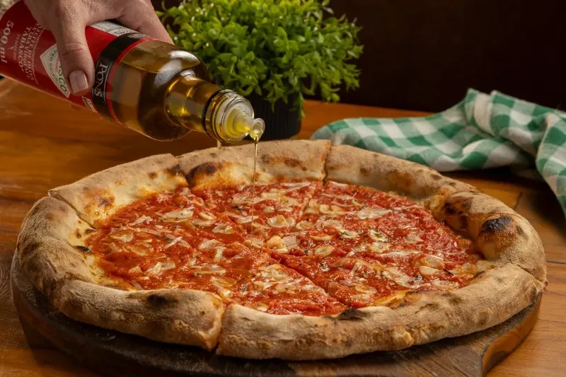 Azeite sendo adicionado à pizza da Varanda 228 sobre tábua de madeira.
