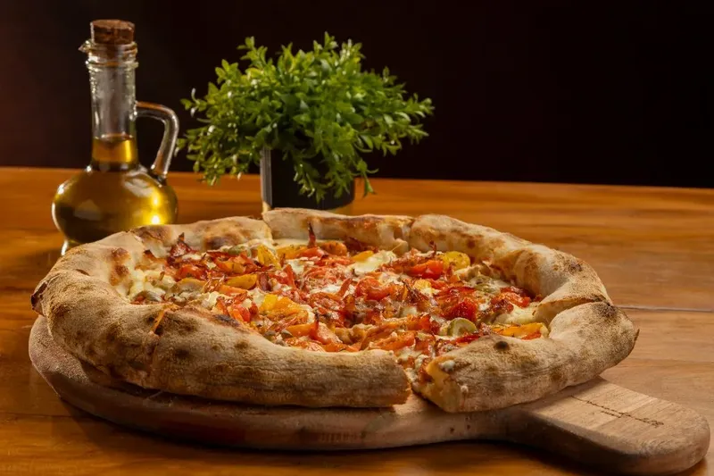 Pizza da Varanda 228 sobre tábua de madeira, em mesa com azeite.