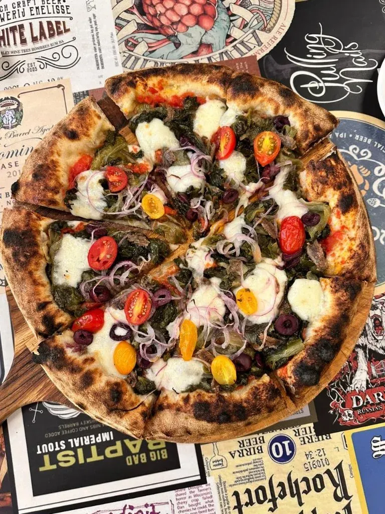 Pizza pronta da Varanda 228 sobre uma pá de madeira, fotografada de cima.