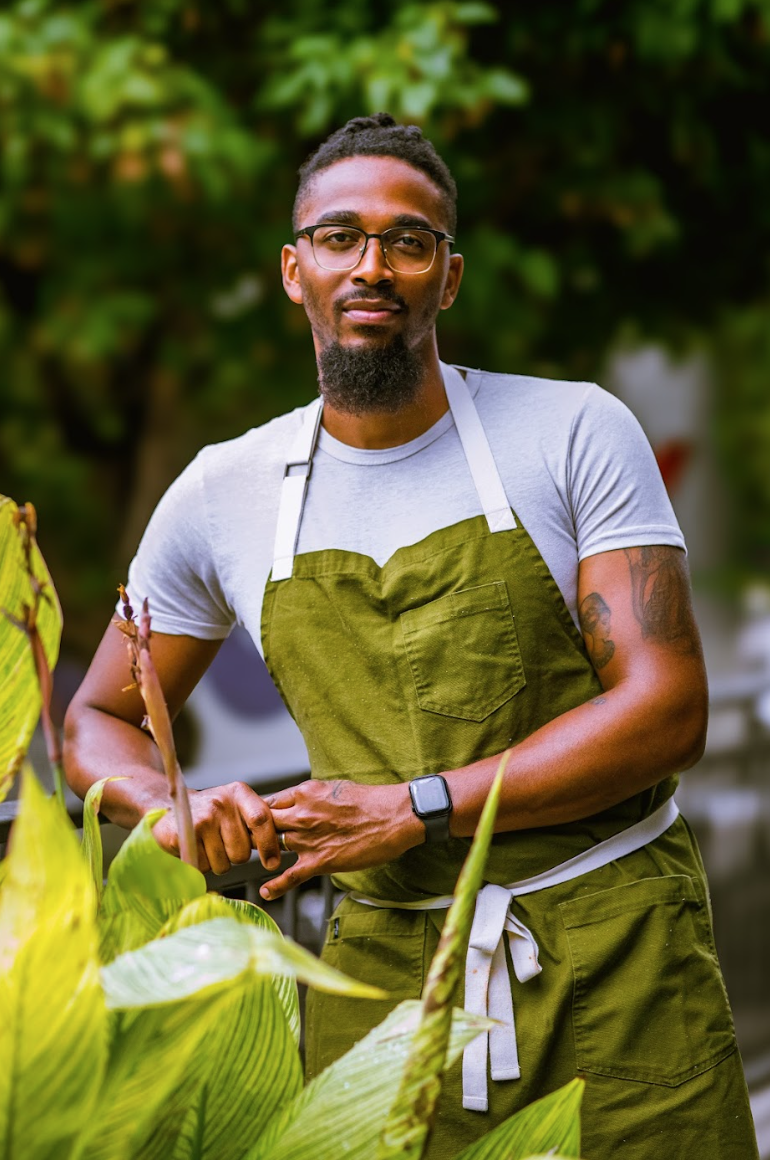 Chef Demetrius Brown standing outdoors in a green apron