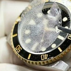Close-up of a luxury watch crystal being wiped with a white cleaning cloth