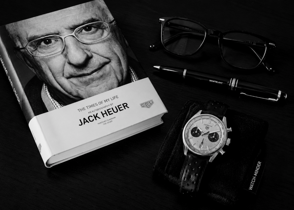 Person wearing a black WATCH-MINDER™ merino wool protector over a luxury rectangular wristwatch on a wooden table with a book