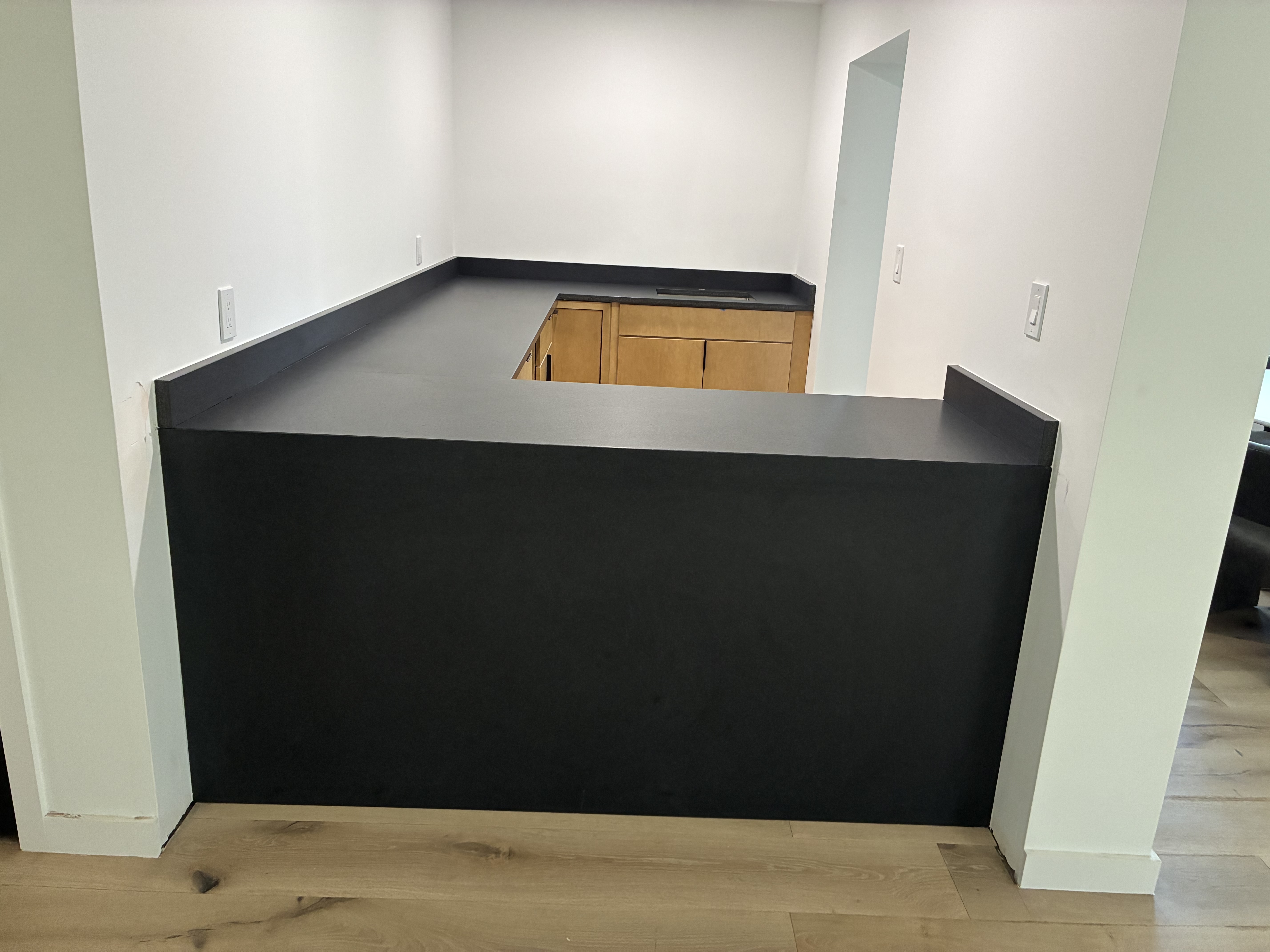 L-shaped kitchen with matte black quartz countertops and light wood cabinetry