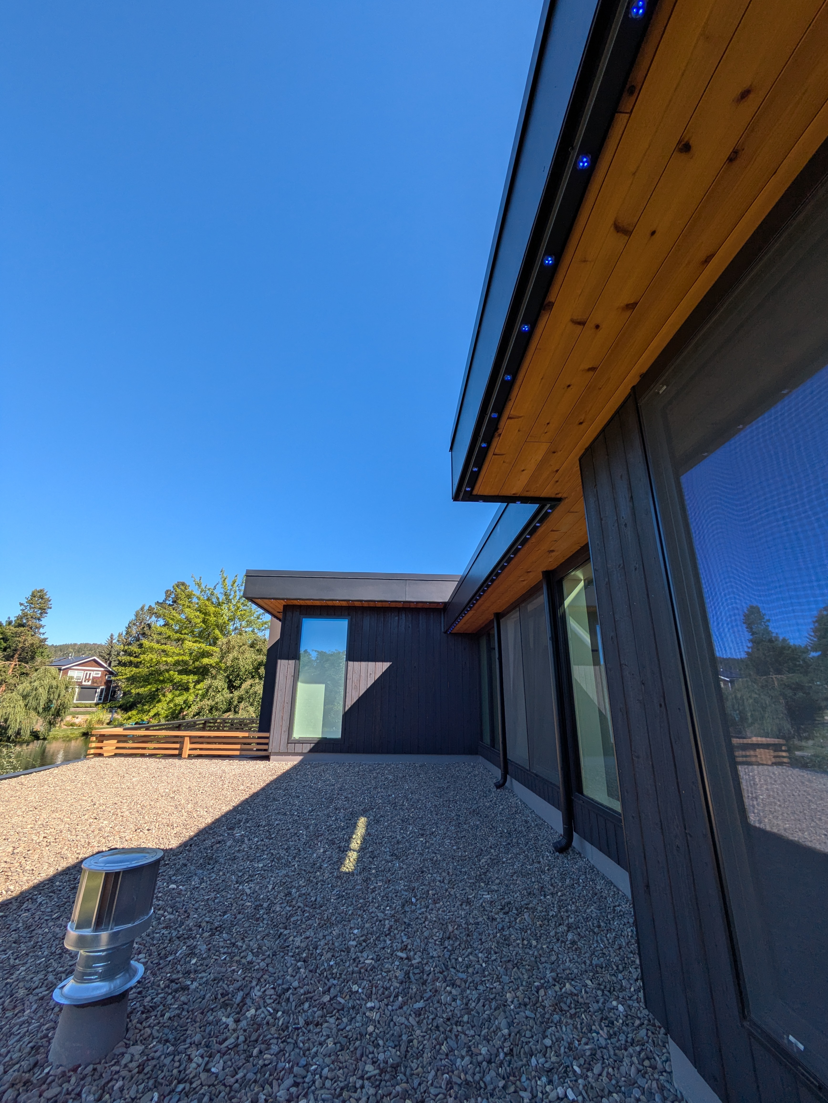 Modern dark-sided home with cedar soffit and blue Gemstone Lights accent lights on rooftop terrace overlooking the river in Bend, Oregon — daytime profile