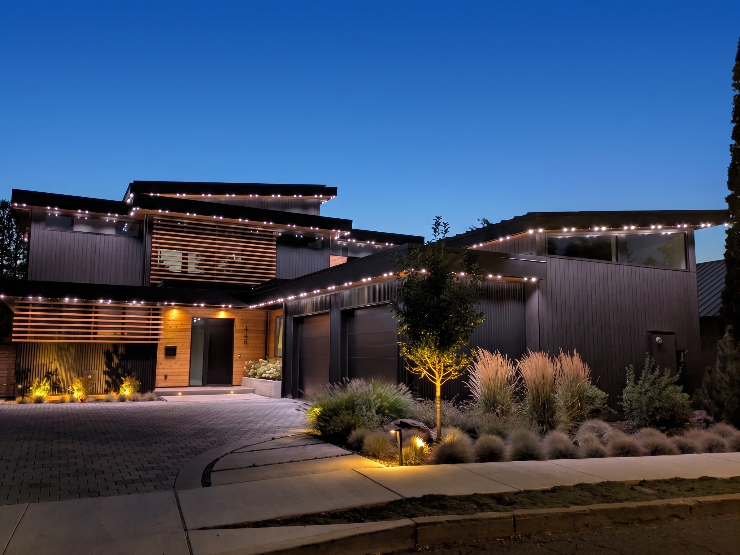 Modern two-story home with warm white Gemstone Lights architectural roofline lighting and wood accents at dusk in Bend, Oregon