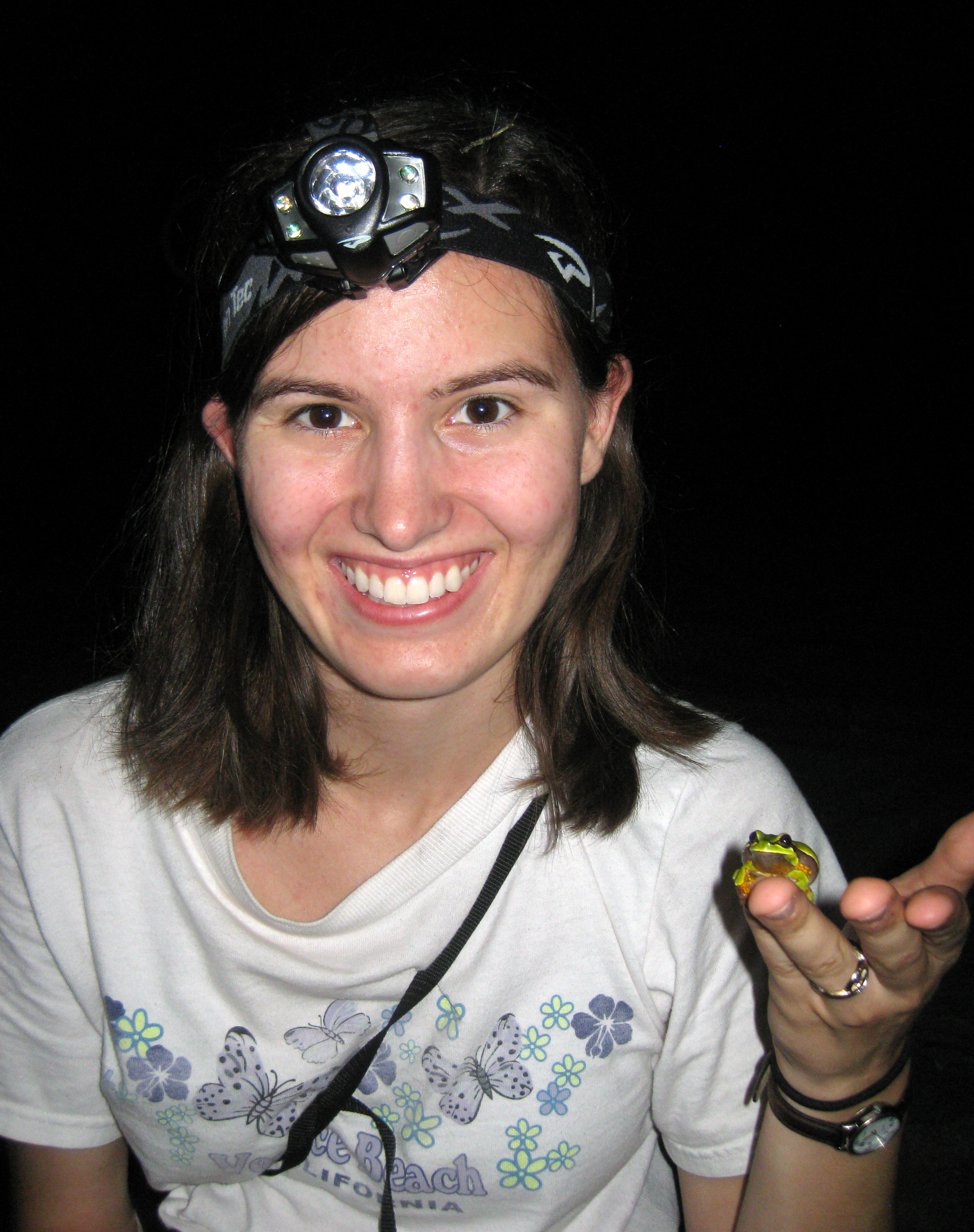 Alexa Warwick holding a green frog illuminated by headlamp at night