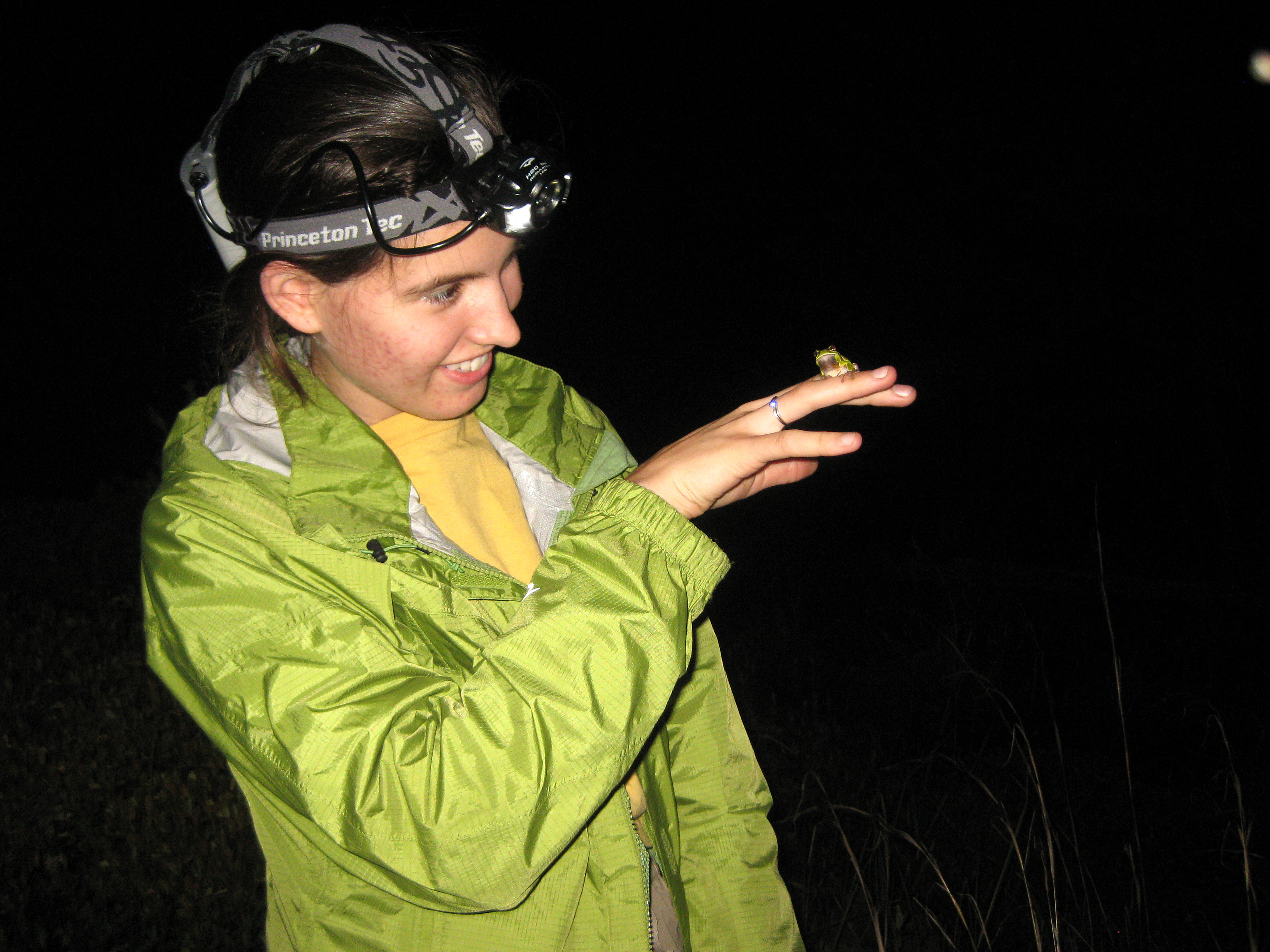 Alexa Warwick with a small green frog on her finger during nighttime fieldwork