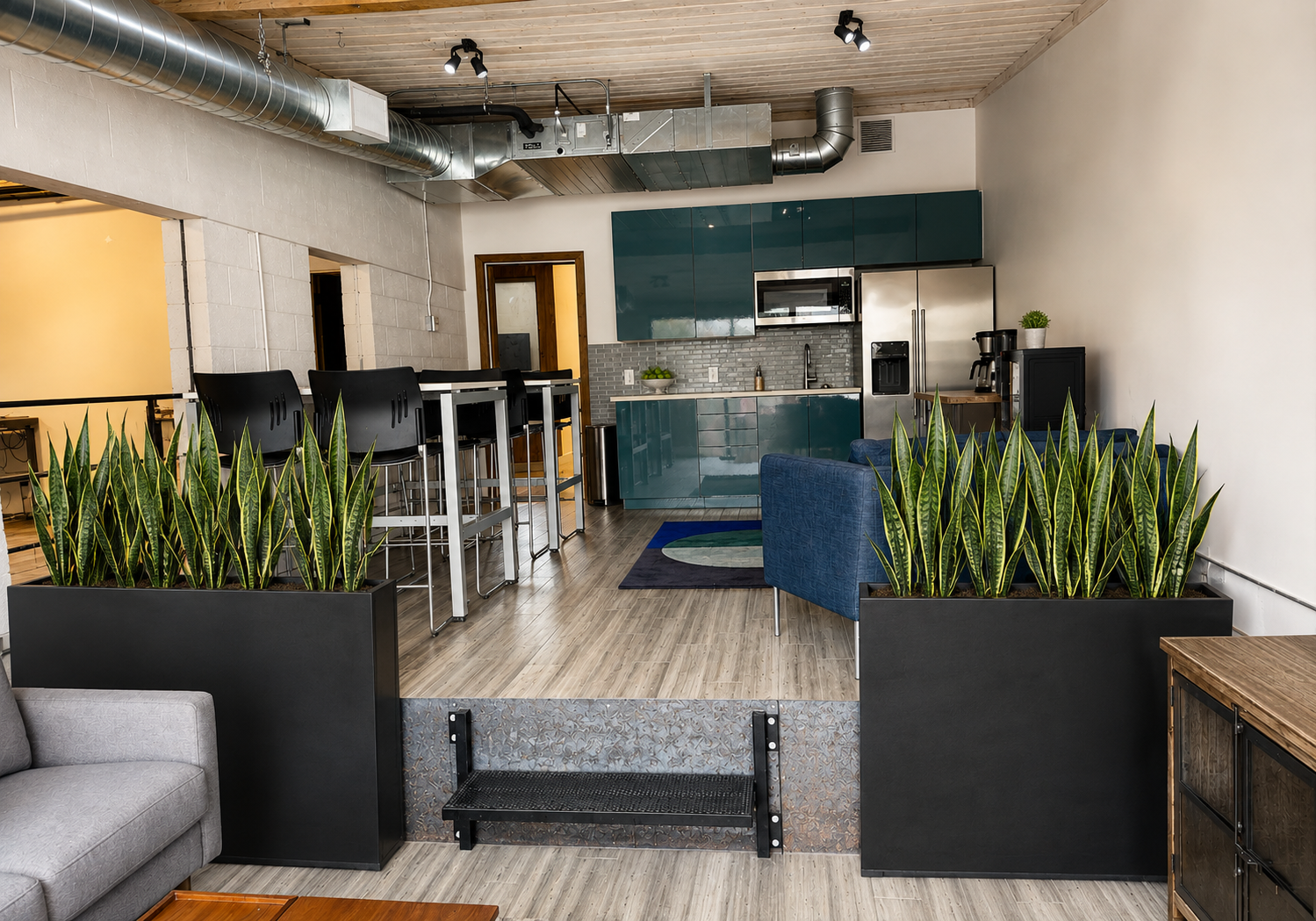 Kitchen collaboration area at The Visionary — teal kitchenette, bar seating, and lounge chair