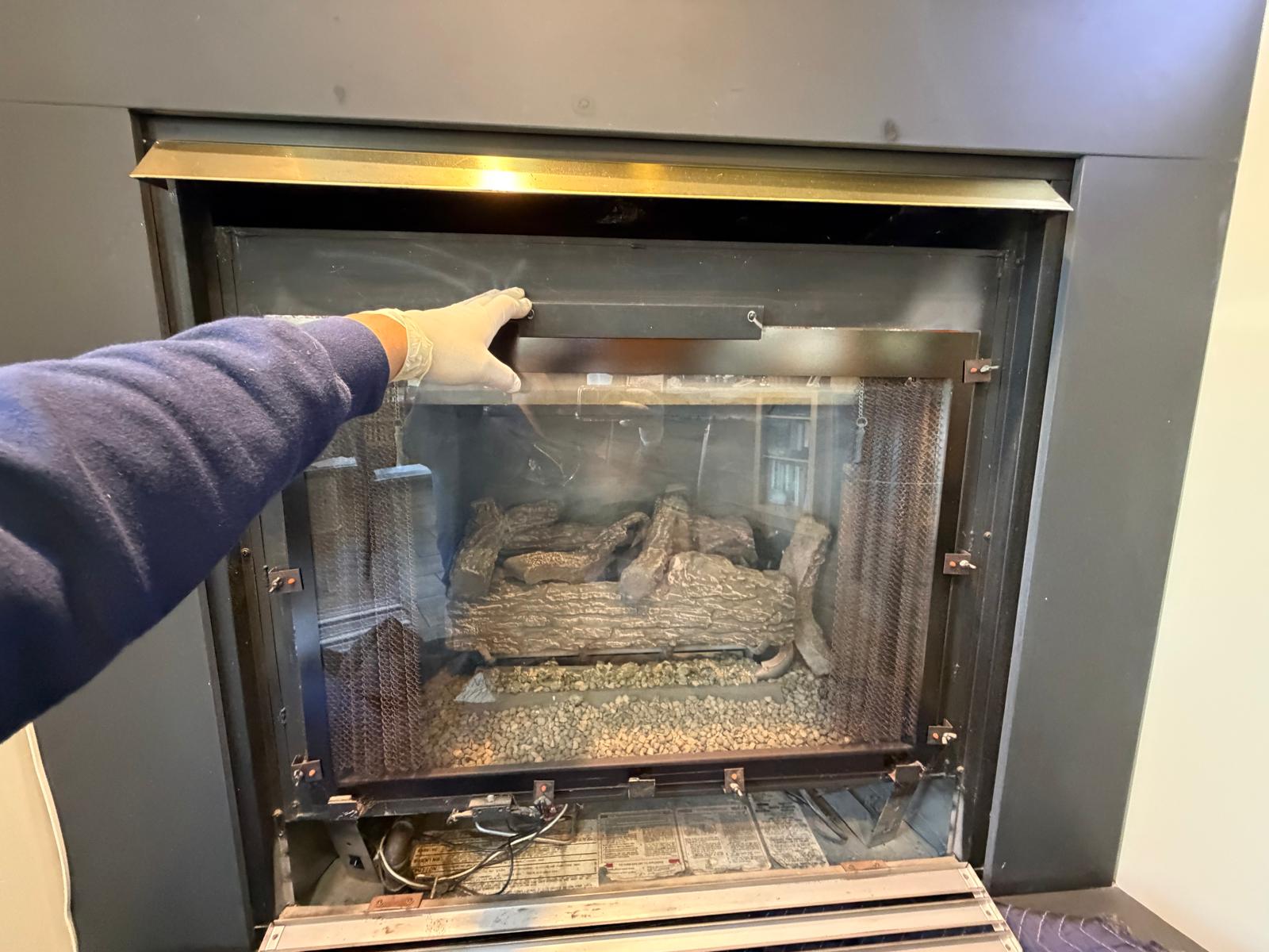 Technician inspecting gas fireplace glass panel during annual maintenance service