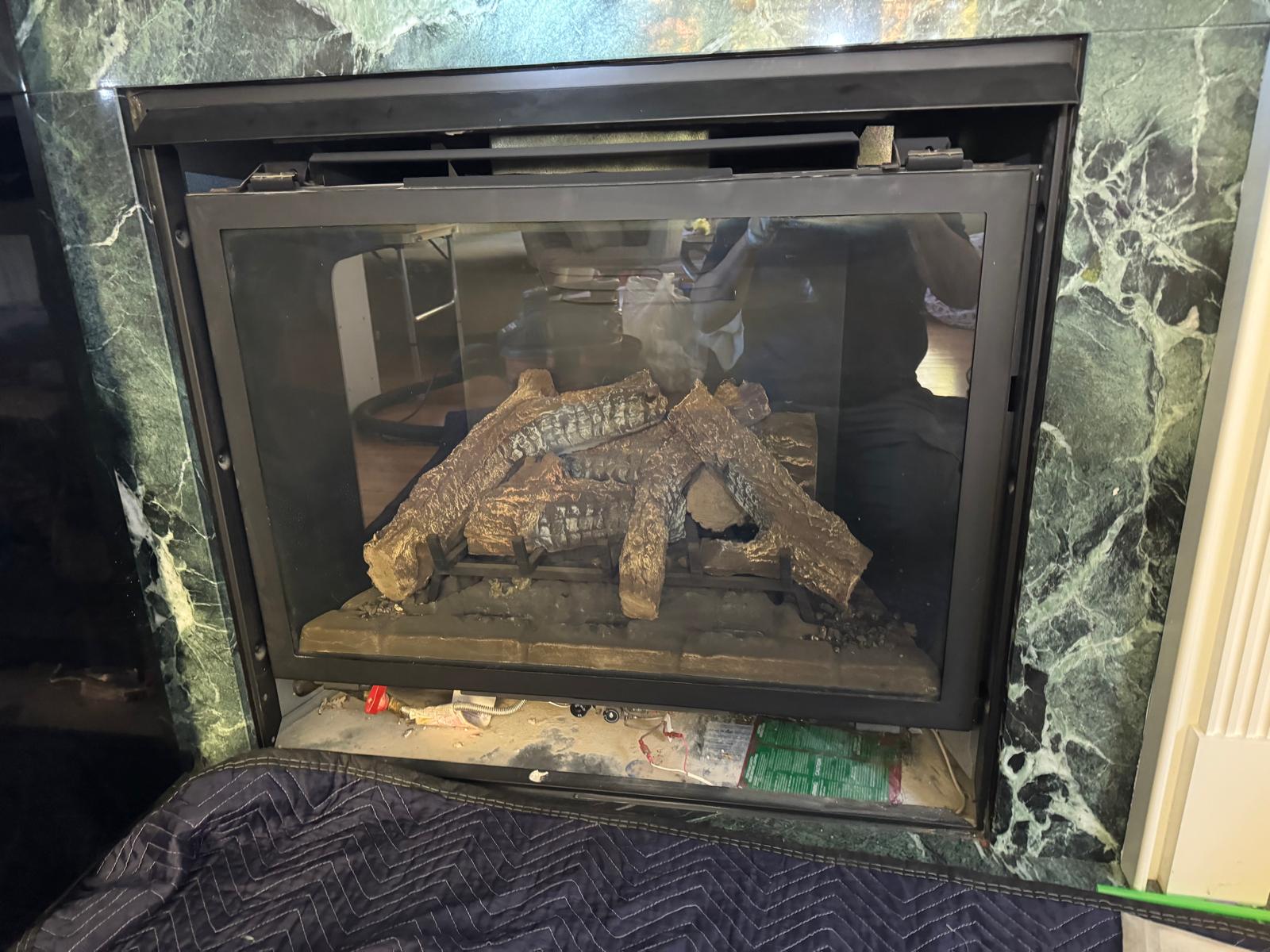Gas fireplace before repair — dirty glass, dusty logs, no flame, debris visible at base