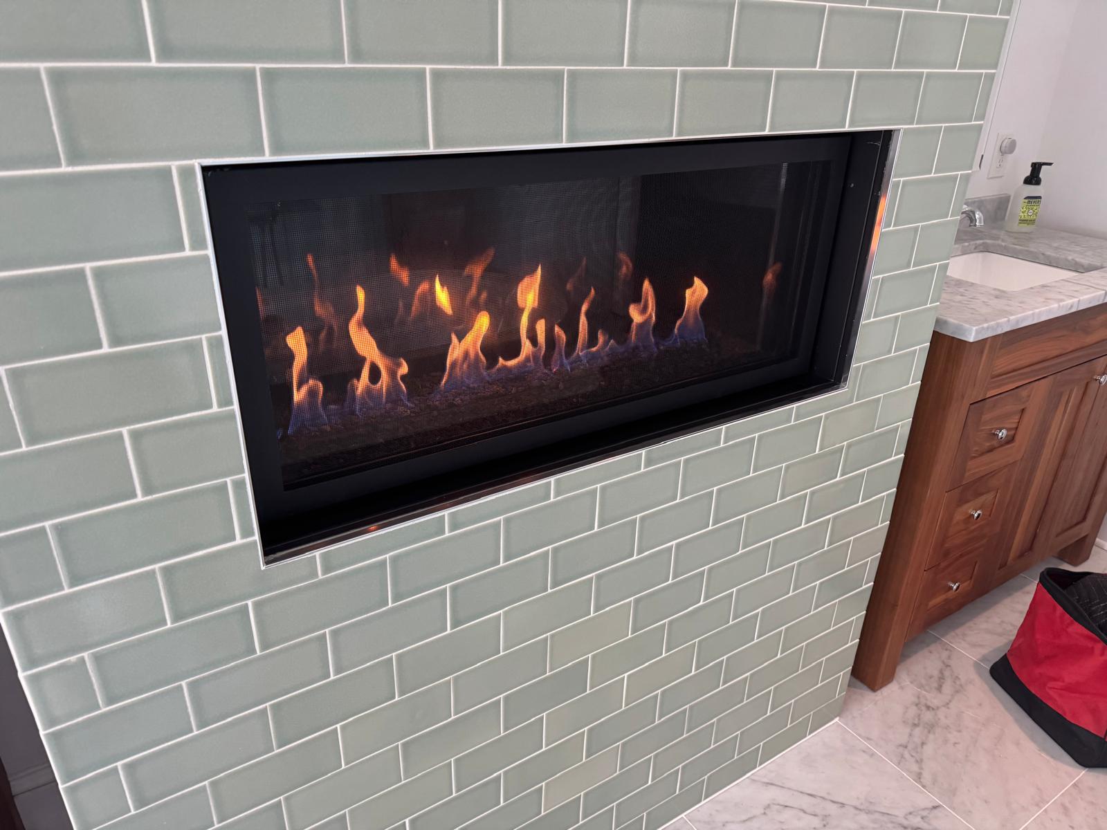 Modern linear gas fireplace with tall flames set in green subway tile wall