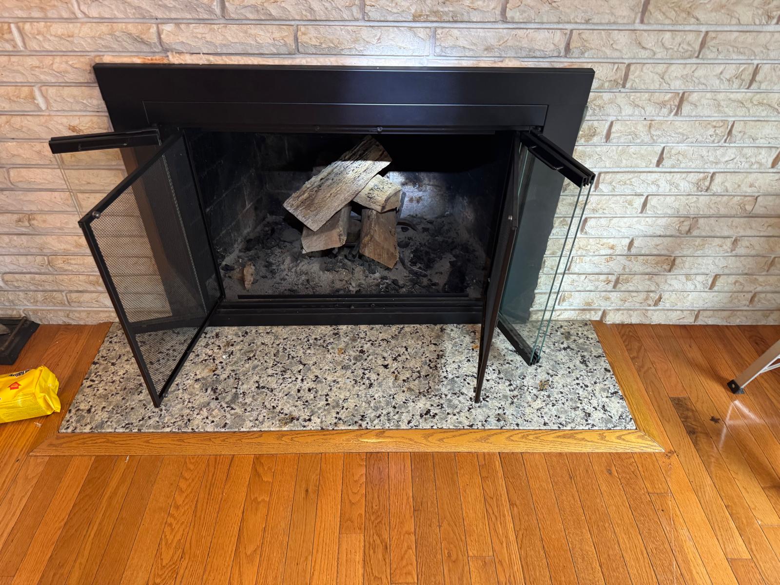 Technician kneeling and inspecting gas fireplace glass panel during service visit