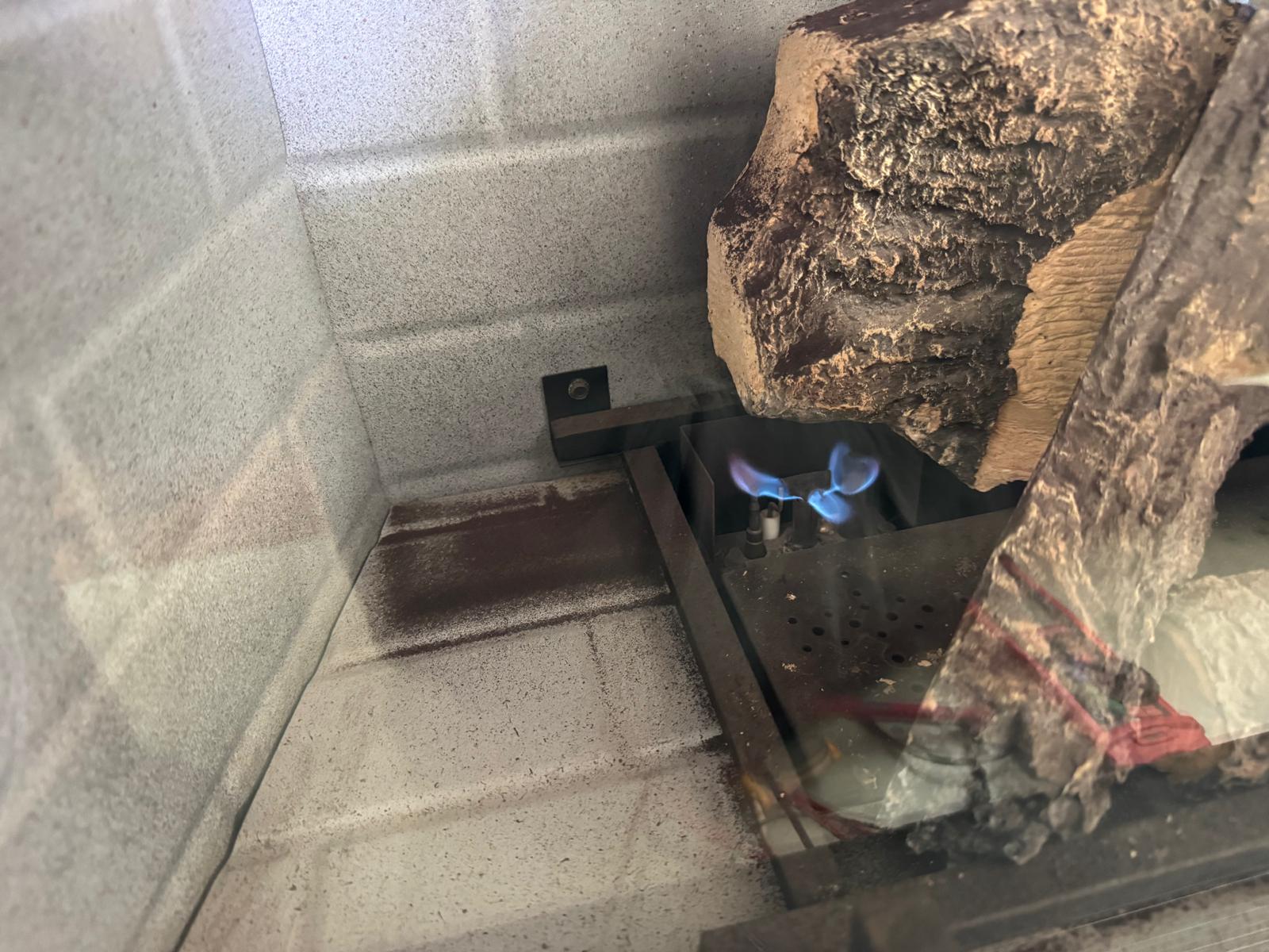 Blue pilot light flame burning inside a gas fireplace firebox during diagnostic check