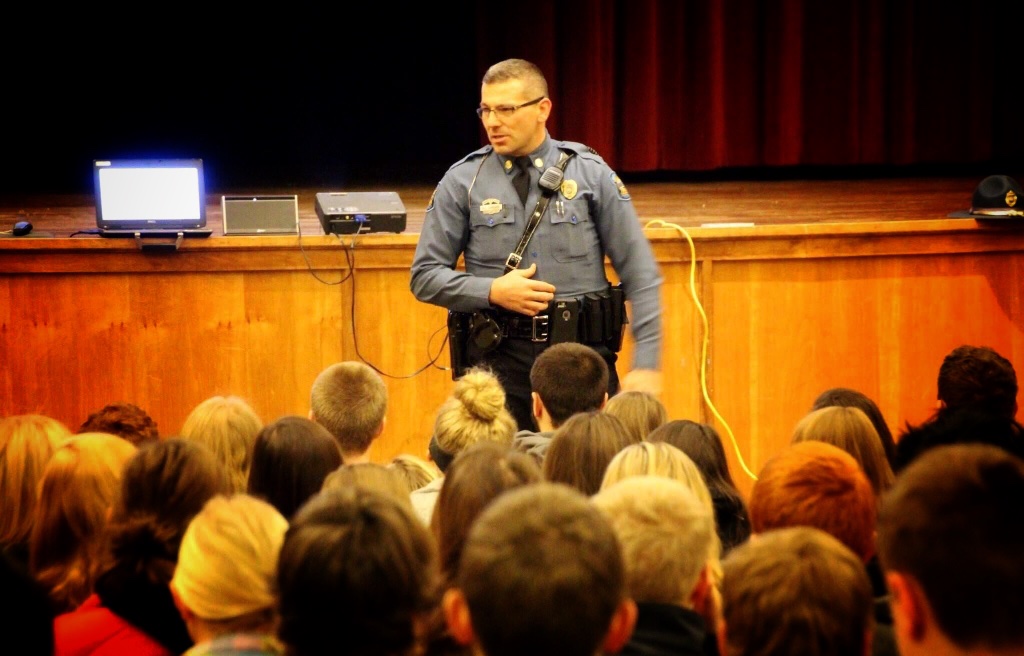 Trooper Ben in uniform speaking to a school assembly