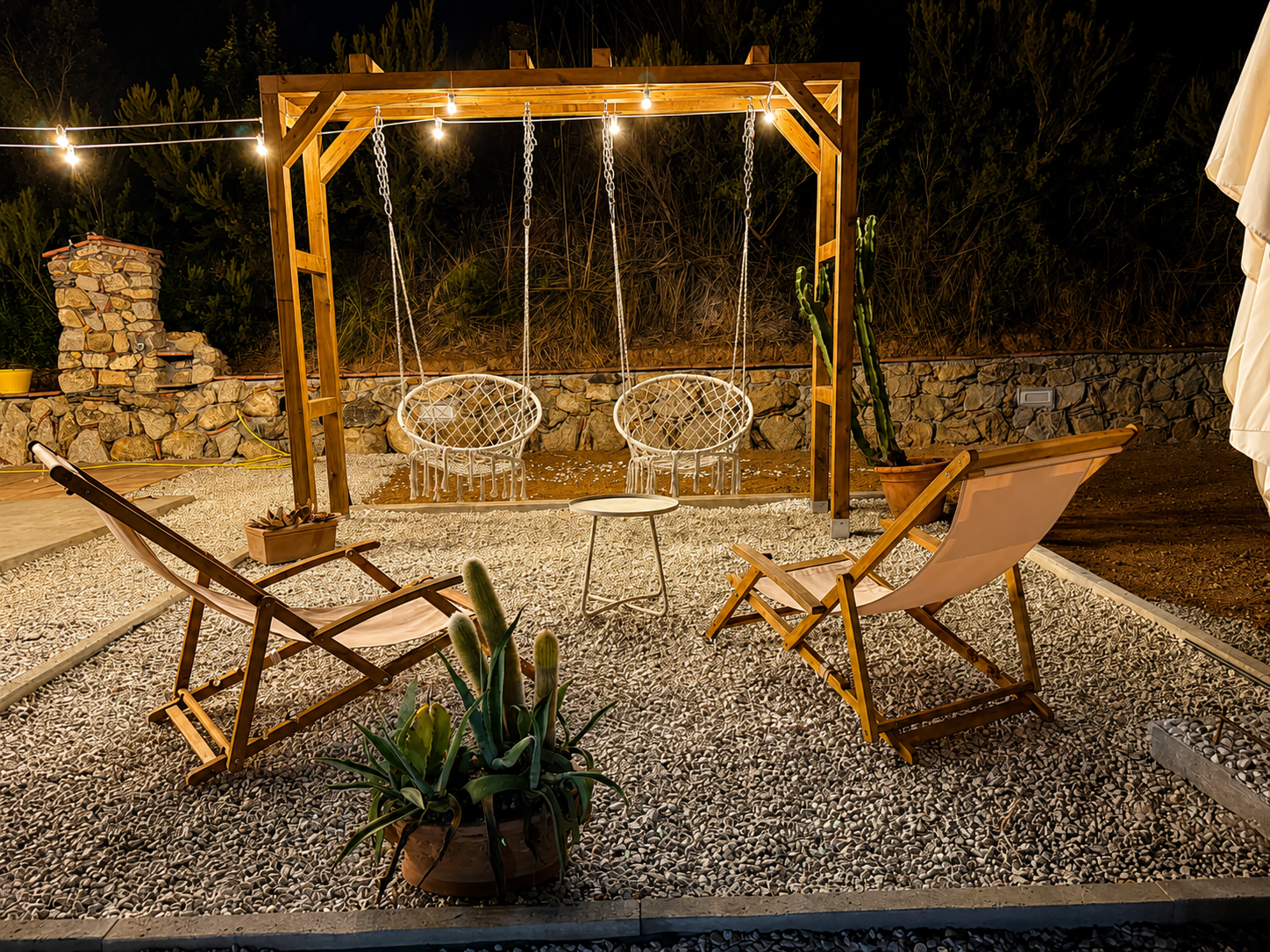 Pergolato con sedie sospese illuminate da luci serali nel giardino di Reale Home a Porto Azzurro